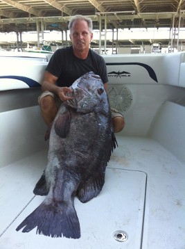 A man on a boat holding a huge fish.