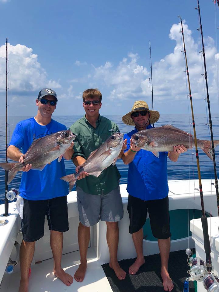 Three men on a fishing boat holding fish