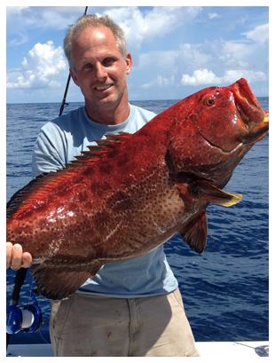 A man on a boat holding a big red fish.